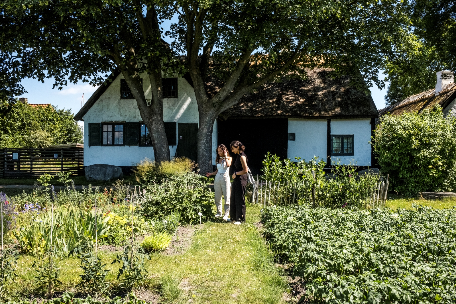 To kvinder i en køkkenhave med gammelt hus i baggrunden